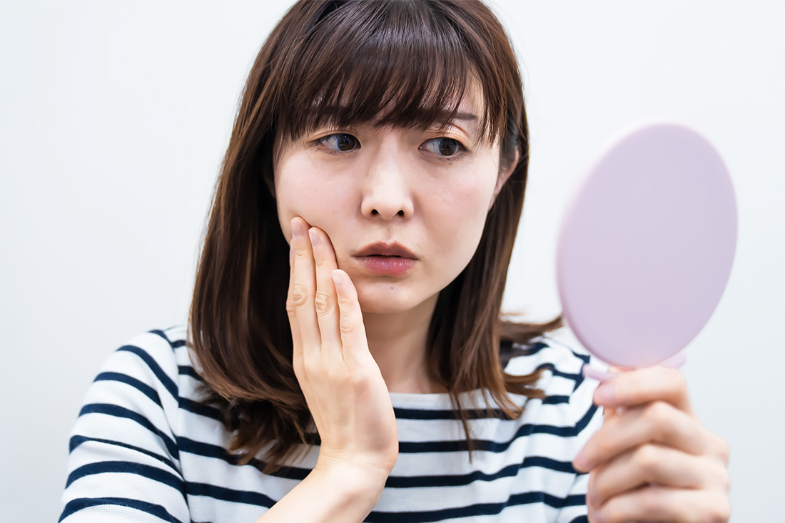 手鏡で顔をみながらそばかすに悩む女性