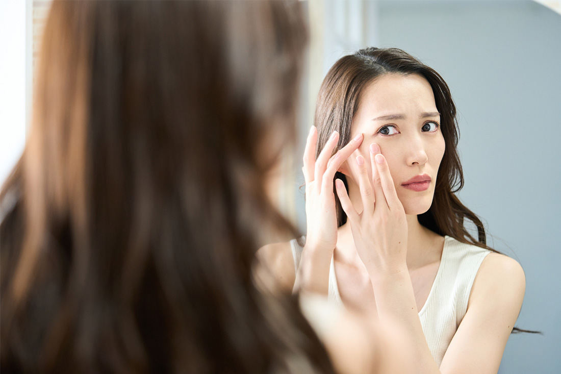 鏡を見て顔のシミに悩む女性