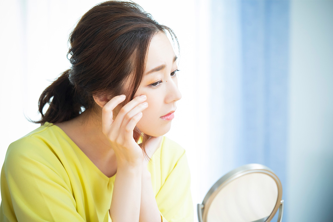 鏡を見ながら顔のシミに悩んでいる女性