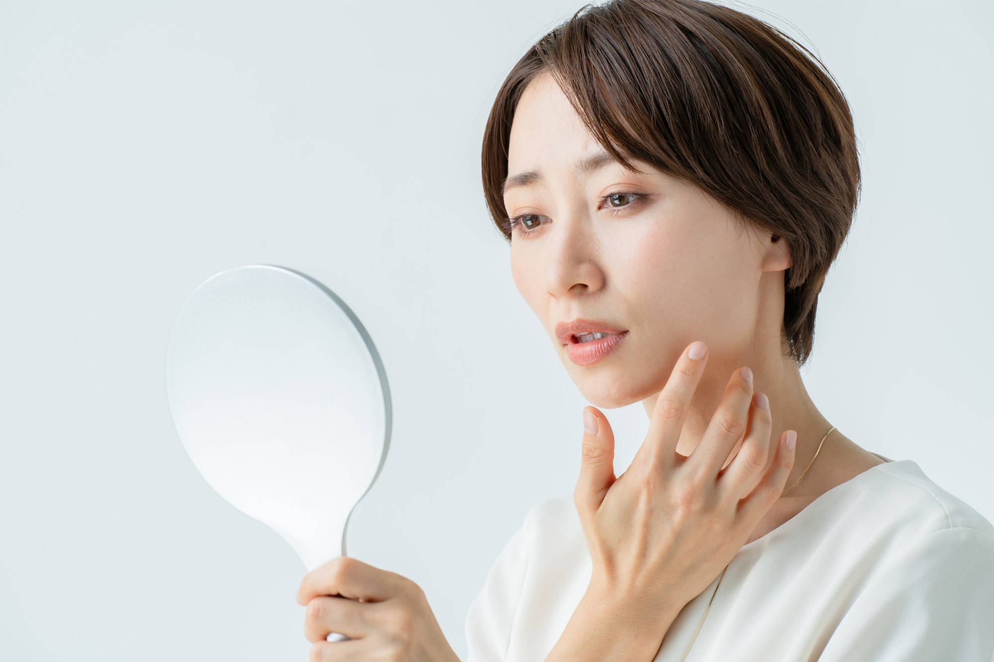 鏡を見て顔のしみを気にする女性