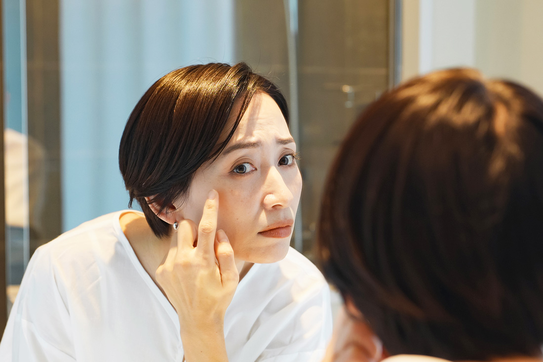 鏡を見て顔にできているシミを気にする女性