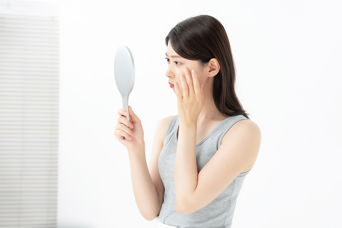 手鏡を見ながら顔にできたシミに悩んでいる女性