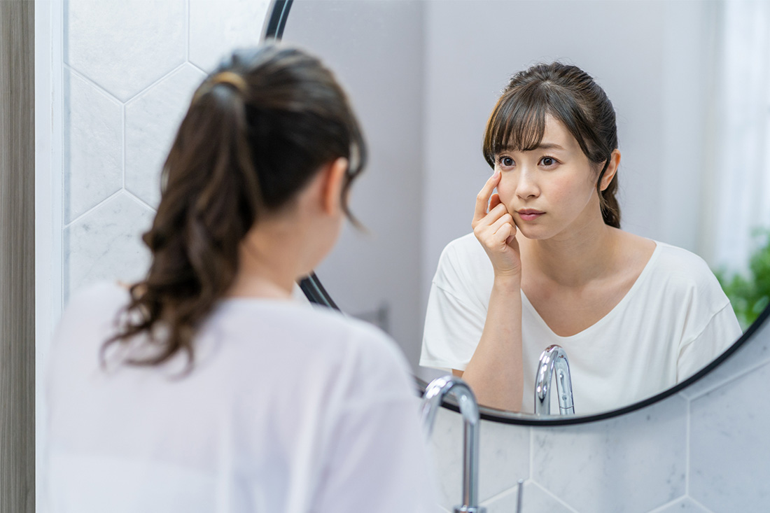 鏡をみて肌のシミを気にする女性